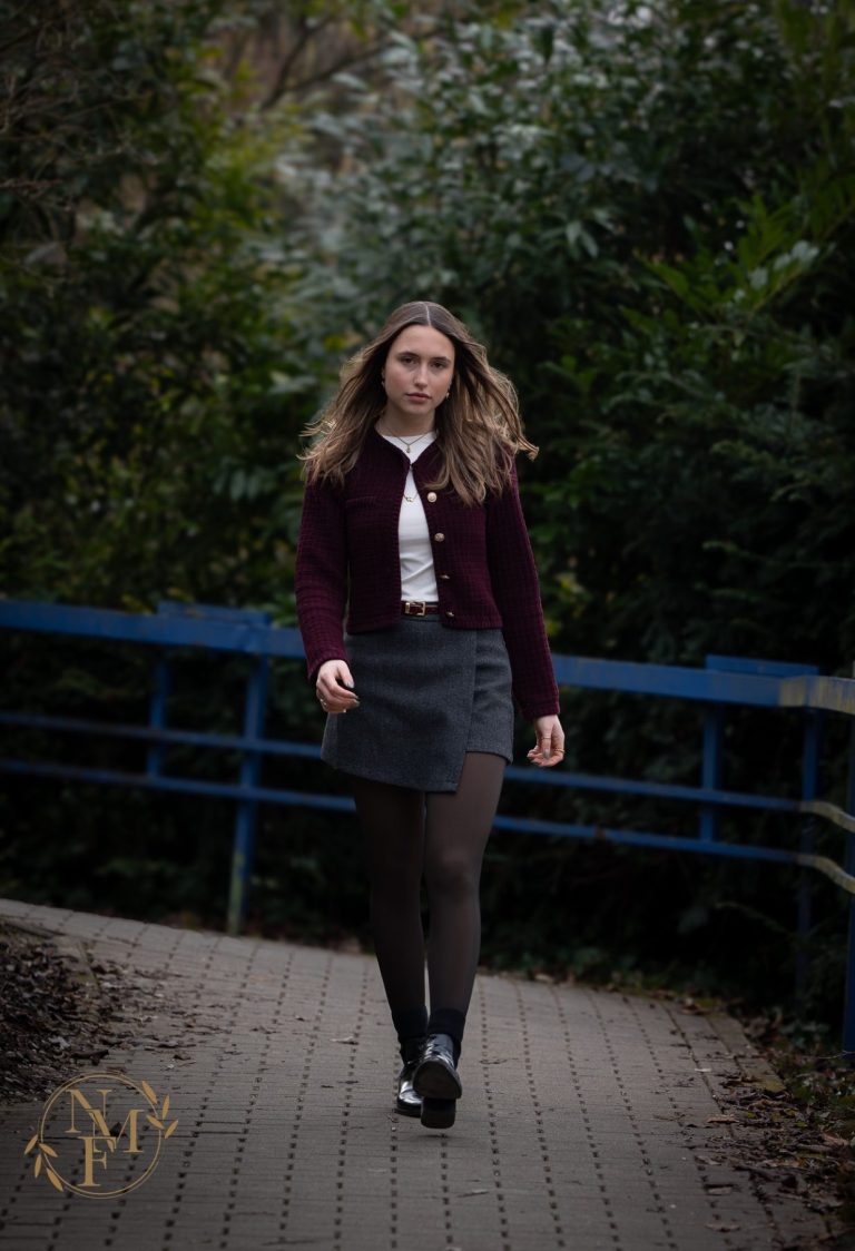 Junge Frau mit lockigem Haar, in einem roten Pulli und Rock, geht auf einem Weg.