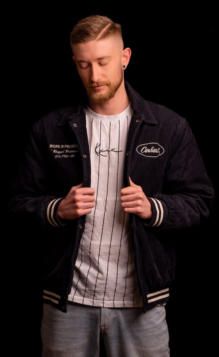 Mann mit kurzem Haar, trägt eine Jacke und T-Shirt, schaut nachdenklich nach unten.