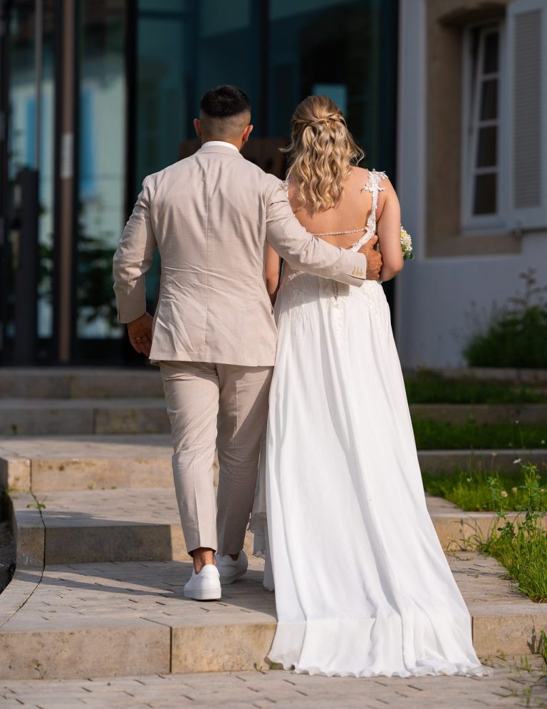 Ein Paar in Hochzeitskleidung geht die Treppe zu einem Gebäude hinauf.