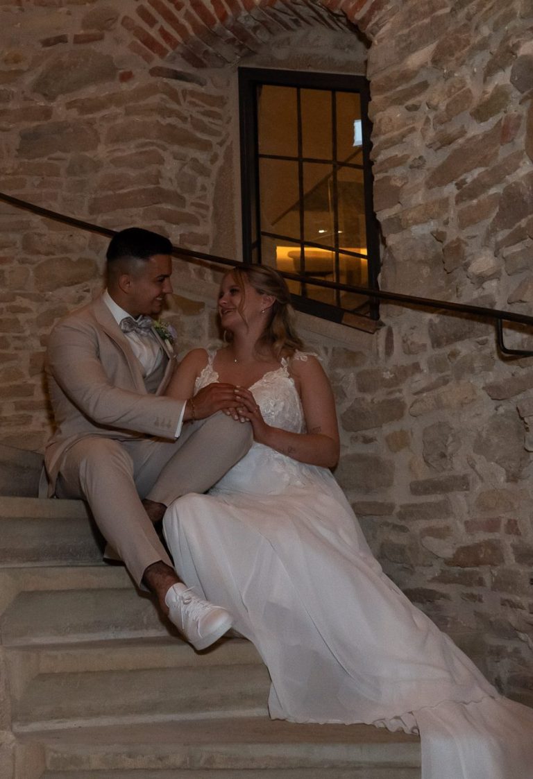 Ein Brautpaar auf einer Treppe, in romantischer Pose, umgeben von Steinmauern.