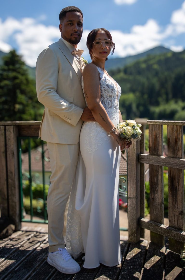 Hochzeitsgesellschaft im Freien, Braut und Bräutigam in eleganter Kleidung, malerische Landschaft im Hintergrund.