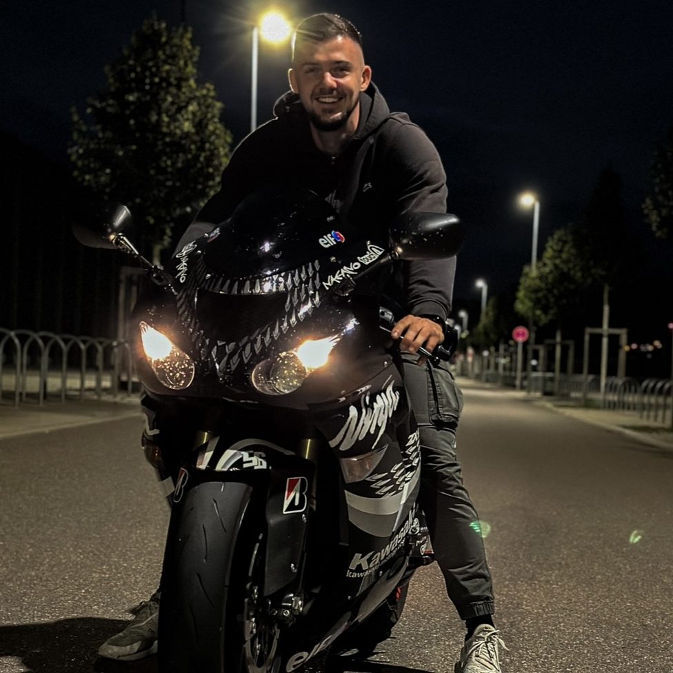 Mann sitzt auf schwarzem Motorrad in der Nacht, umgeben von Straßenlaternen.