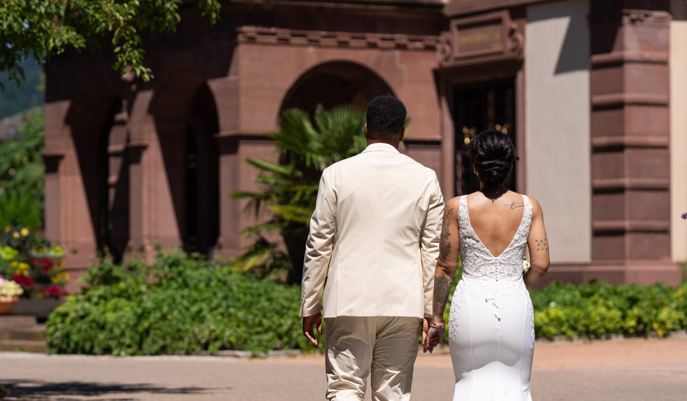Hochzeitspaar, von hinten gesehen, geht Hand in Hand in einem Garten.