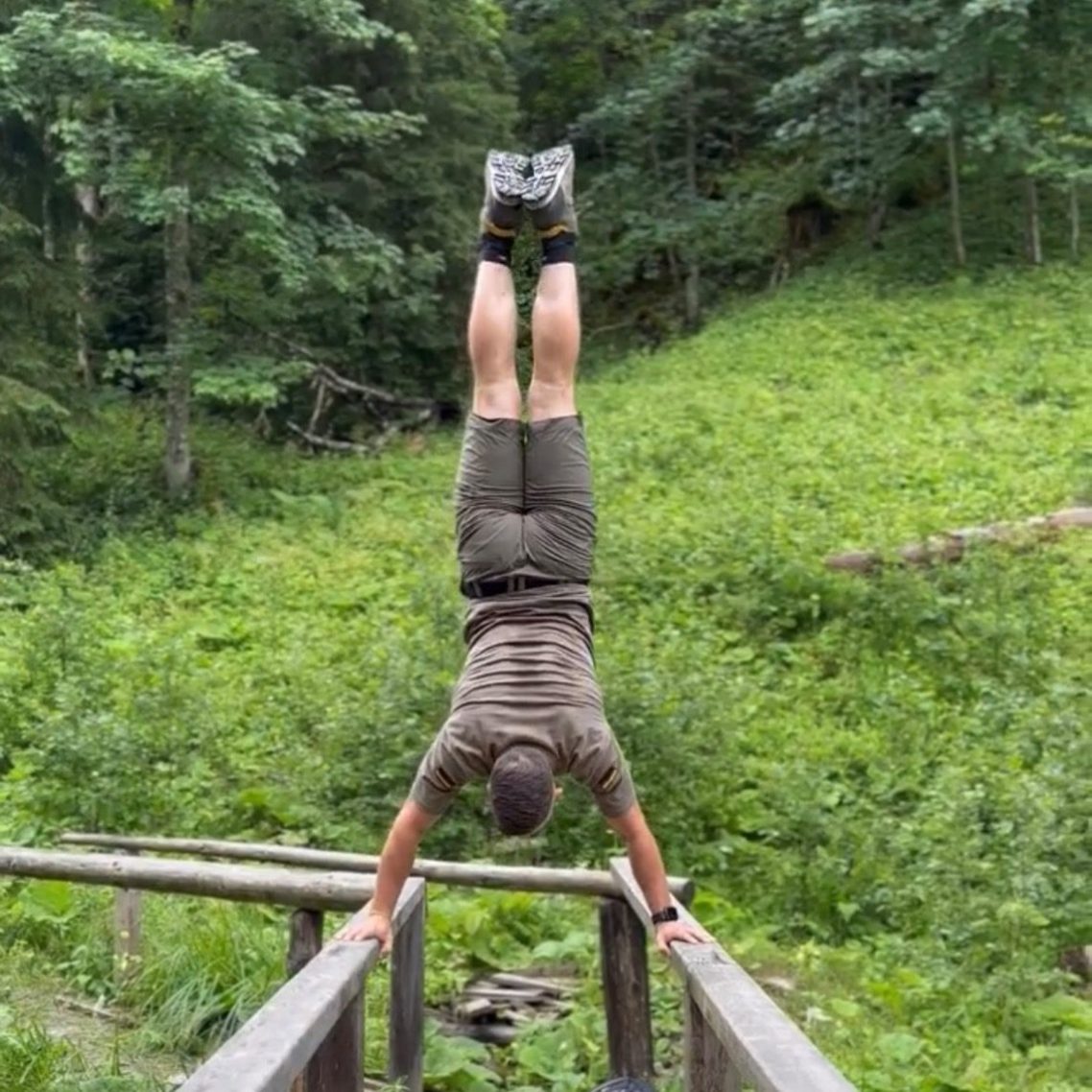 Mann macht einen Handstand auf einer Holzbrücke in der Natur.